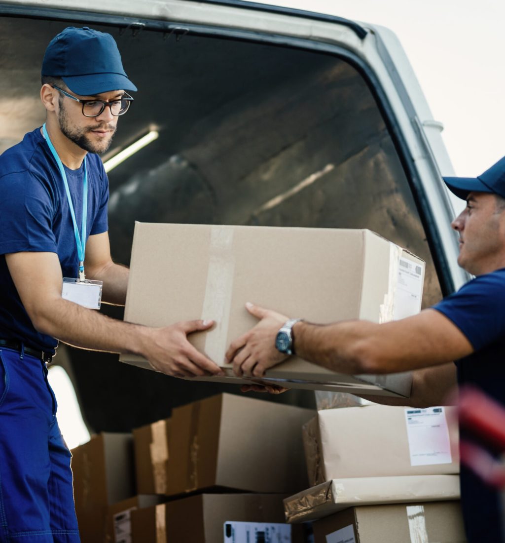 Delivery men loading carboard boxes in a van while getting ready for the shipment.
